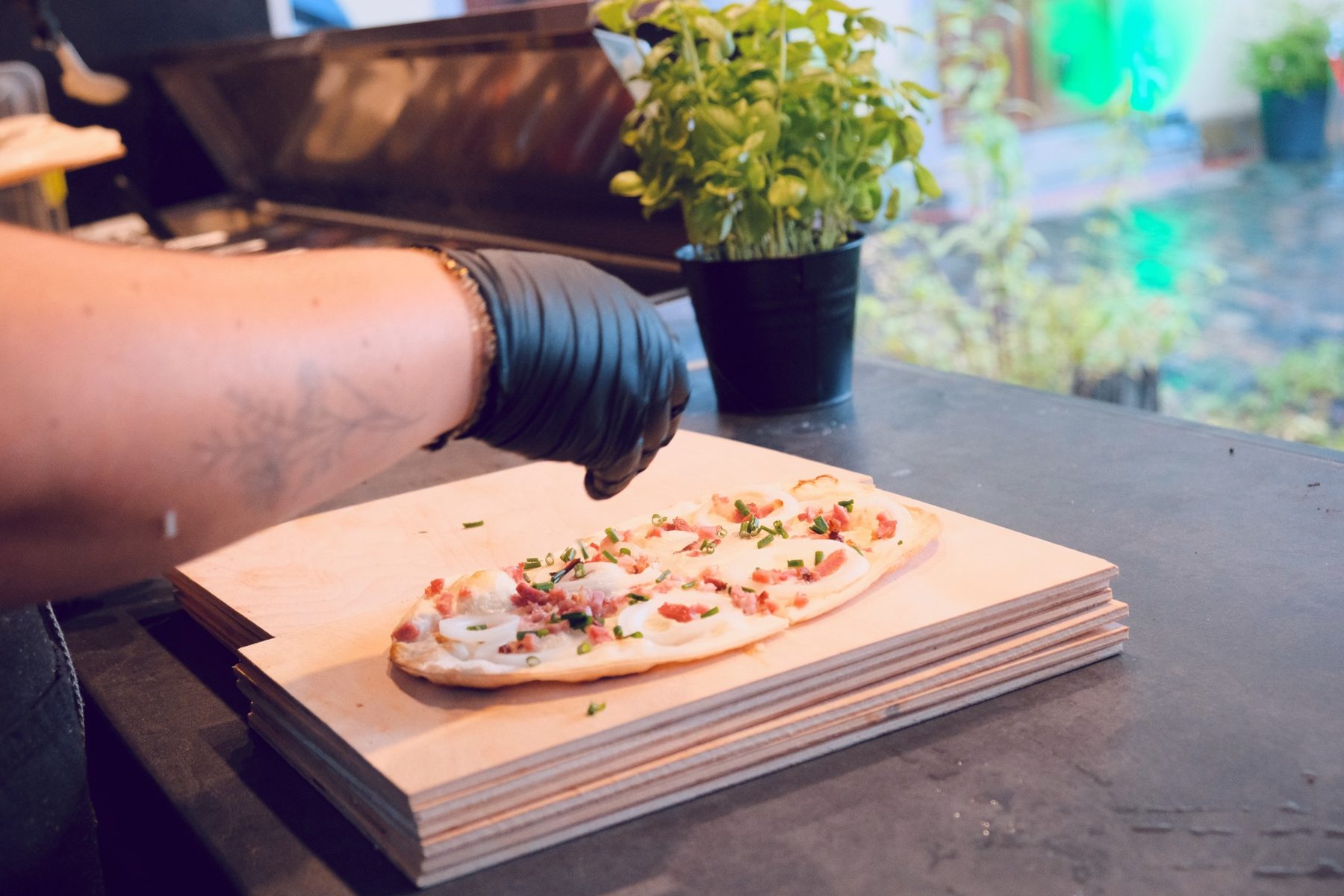 Ein fertig belegter Flammkuchen wird beim Catering auf ein Holzbrett gelegt, daneben frischer Basilikum