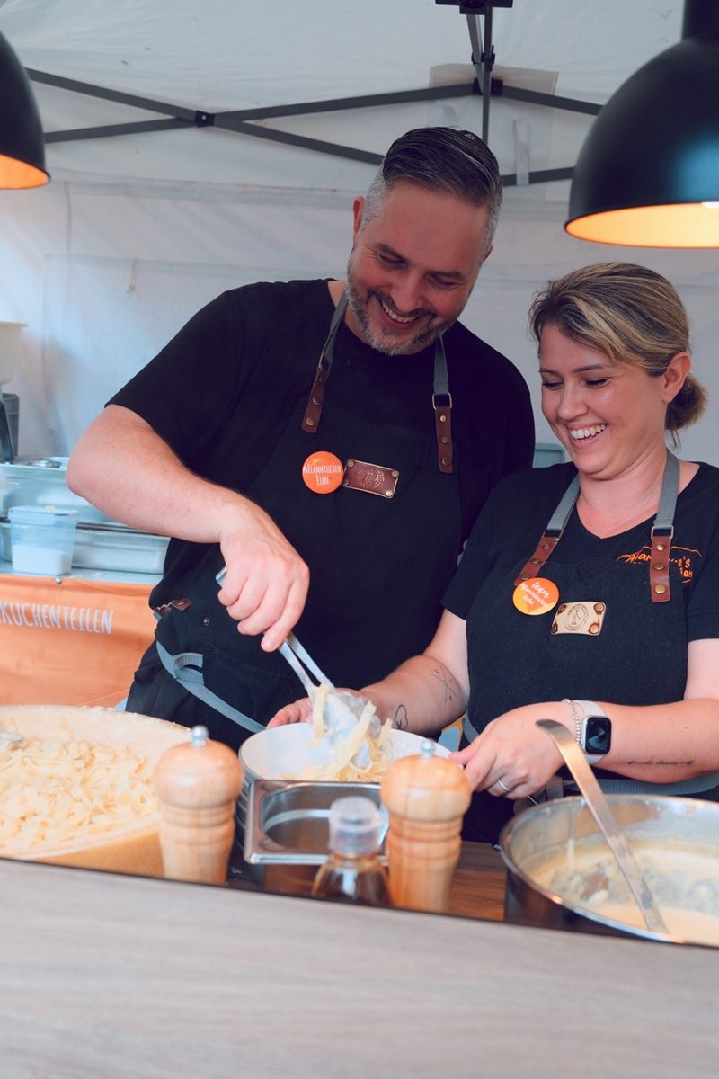 Zwei Mitarbeitende an der Pastastation beim Catering – links der halbe Parmesanlaib, in dem die Pasta verfeinert wird