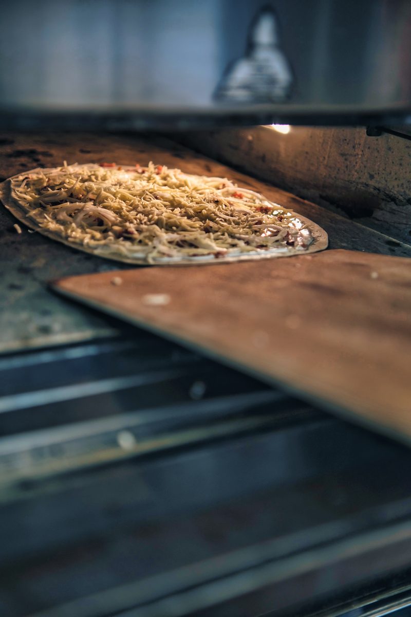 Ein fertig belegter Flammkuchen auf dem Schieber, kurz vor dem Ofen