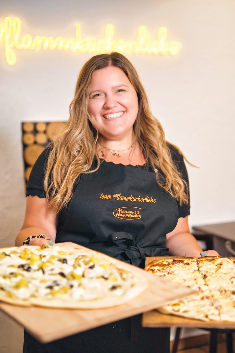 Ein Teammitglied mit zwei fertigen Flammkuchen unter der Neonschrift #flammkuchenliebe